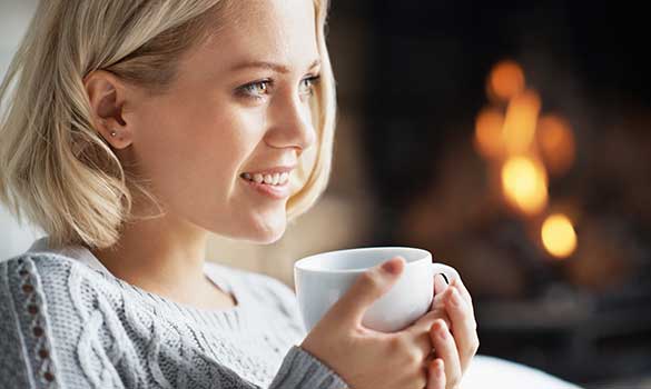 woman drinking warm beverage in front of fireplace and chimney